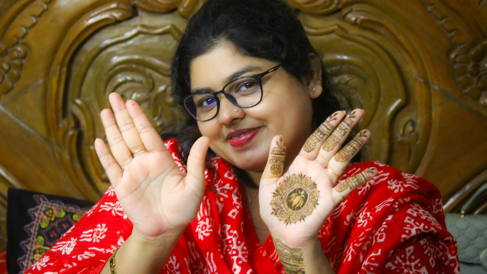A smiling Indian woman in a red bandhani dupatta showing mehndi art on her palms