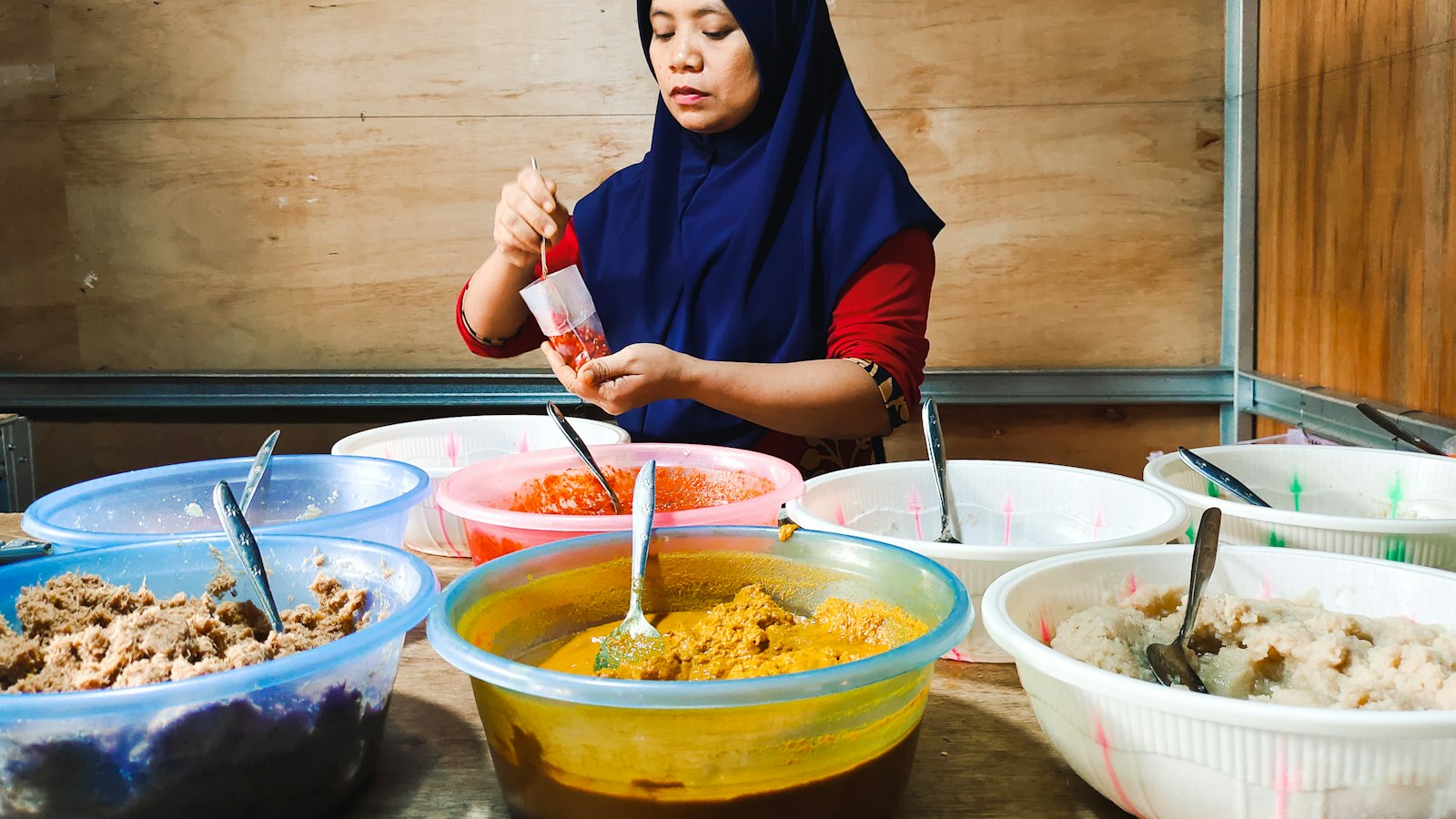A woman in a hijab preparing food behind a counter of bowls at her home kitchen business